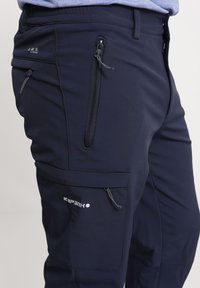 Marineblauwe Softshell-Hosen mit mehreren Reißverschlusstaschen, einem elastischen Bund und Logo-Details. Glatte Textur und schlankes Design für zusätzlichen Komfort.