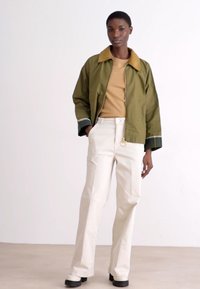 Jacket corta verde-azeitona com colarinho bege, combinado com calças de cintura alta bege e sapatos pretos robustos. Design minimalista com linhas limpas.