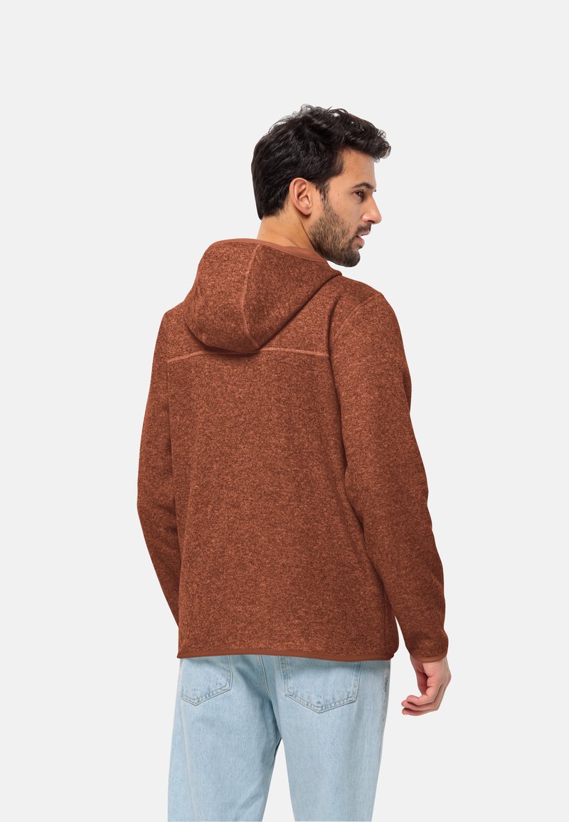 Brązowy dzianinowy hoodie z fakturowanym wzorem, z kapturem, długimi rękawami i luźnym krojem. Połączenie z jasnobłękitnymi dżinsami dopełnia stylizację.