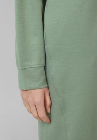 Langärmliges Kleid aus weichem, mintgrünem Stoff. Es bietet eine lockere Passform, saubere Nähte und eine subtile Textur, mit einem runden Ausschnitt.