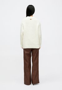 Κρεμ πλεκτή μπλούζα με υ�φασμάτινο σχέδιο, με στρογγυλή λαιμόκοψη και χρυσή λεπτομέρεια στην πλάτη, συνδυασμένη με καφέ φαρδιά παντελόνια από συνθετικό δέρμα.