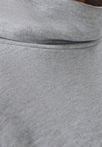 Grauer Pulloverstoff mit strukturiertem Strickdesign. Verfügt über einen hohen, gefalteten Kragen und eine glatte Oberfläche. Sichtbare Nahtdetails entlang der Kanten.