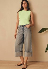 Top sin mangas en verde menta combinado con unos vaqueros de pierna ancha en azul claro con dobladillo. Sandalias con tiras metálicas completan el atuendo.