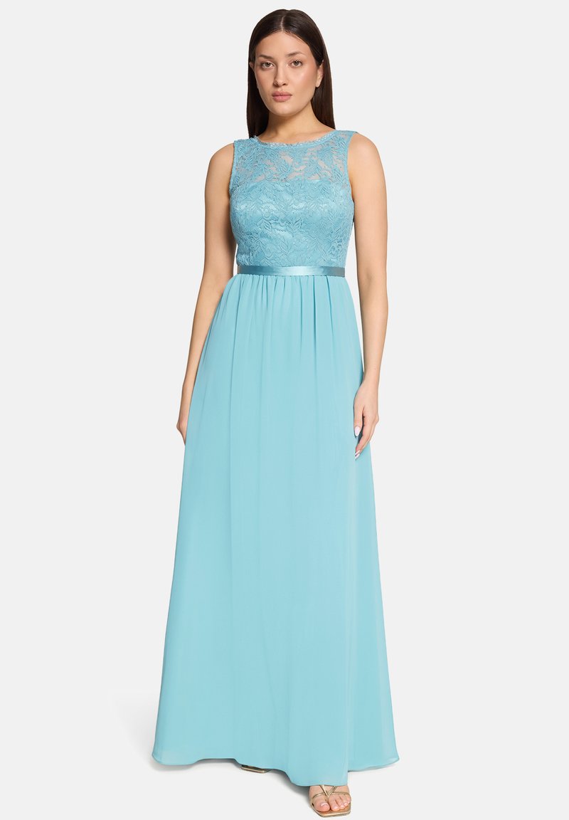 Femme portant une robe bustier en dentelle bleu clair avec une ceinture en satin, debout devant un fond blanc uni.