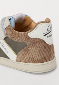 Baskets en corduroy marron avec accents blancs, dotées d'un col rembourré et de panneaux latéraux texturés. Semelle résistante avec un léger détail de couture.