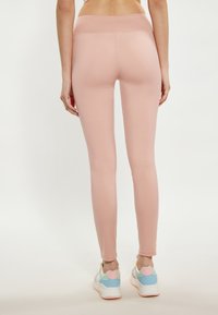 Leggings rosa con una texture liscia e elastica. Presentano una vita alta e un design alla caviglia, abbinati a sneakers multicolori.