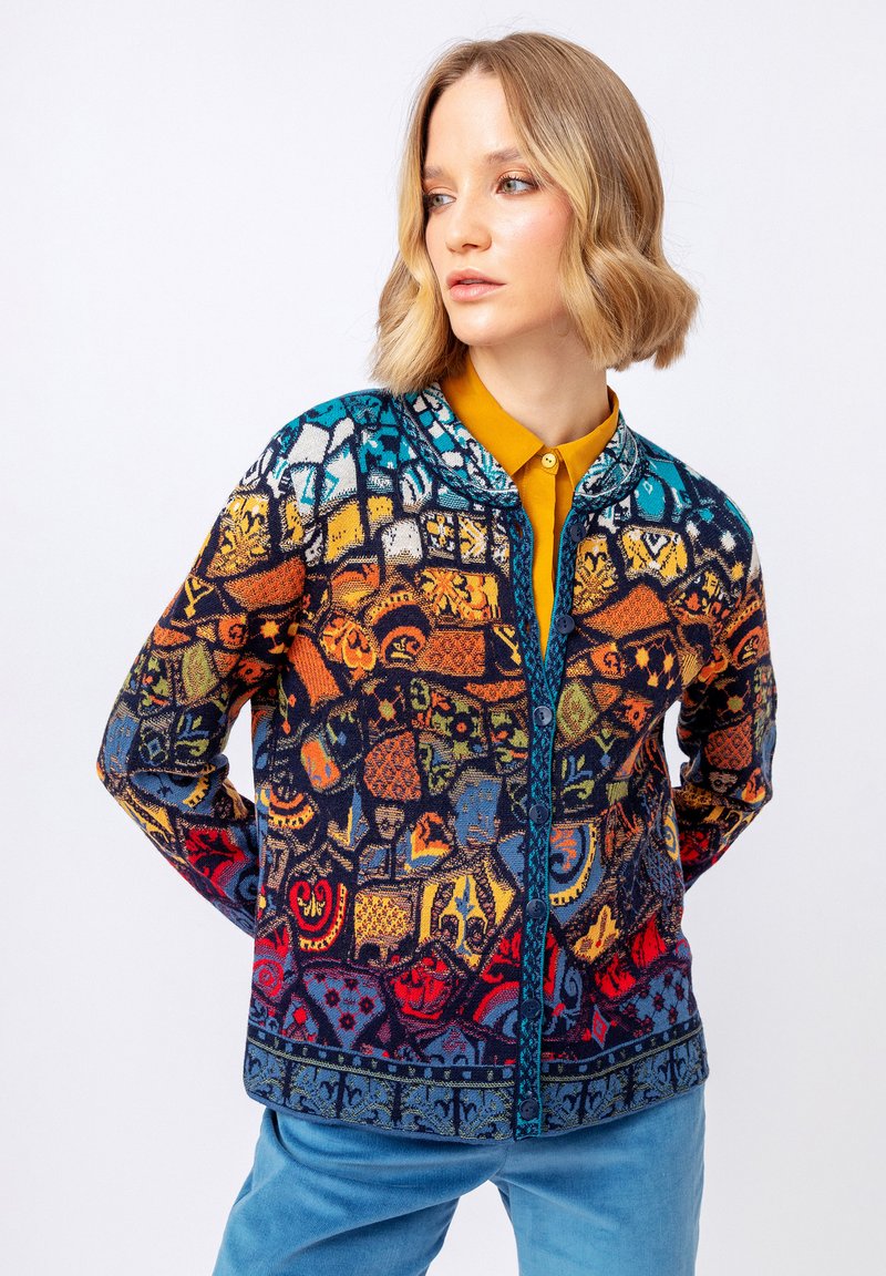 Barevný pletený kardigán s mozaikovým vzorem různých tvarů. Modré, oranžové a červené tóny s předním zapínáním na knoflíky a kontrastním lemem.