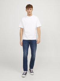 Tricou alb din bumbac, cu mâneci scurte, asortat cu blugi slim-fit de culoare bleumarin și adidași bleumarin cu talpă albă. Design simplu, croială lejeră.