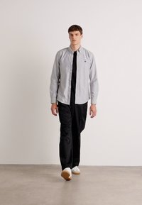 Lichtgrijze lange mouwen overhemd met knopen over een zwart T-shirt, gecombineerd met zwarte broek en witte sneakers. Eenvoudig ontwerp met een standaard pasvorm.