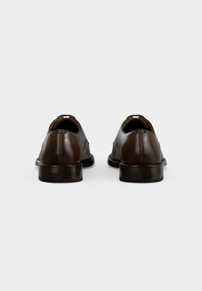 Paire de chaussures habillées en cuir marron vues de dos avec des talons bas et une finition polie lisse sur fond blanc.