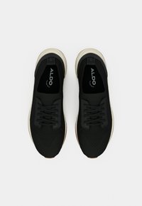 Chaussures de sport noires avec une tige texturée, des lacets plats, des semelles rembourrées et des accents blancs ; logo visible sur les semelles intérieures.