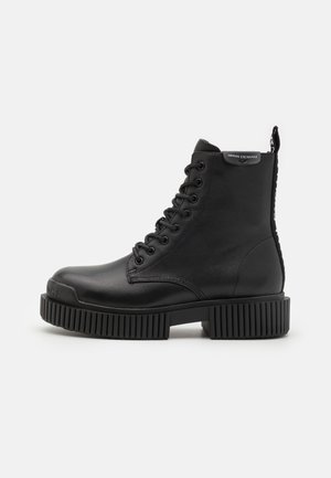 Bottines en cuir noir, avec une semelle épaisse et rainurée, des lacets à l'avant et une languette à l'arrière ornée d'un logo.