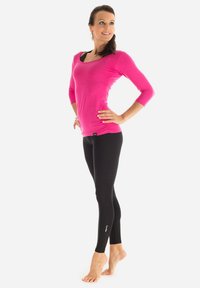 Fuchsia långärmad topp med rundad urringning, tillsammans med svarta leggings med en figurnära design och vitt broderat logotyp nära vristen.