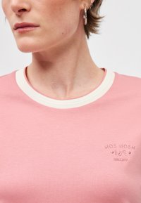 Ροζ βαμβακερό μπλουζάκι με στρογγυλή λαιμόκοψη και κρεμ λωρίδα. Διαθέτει διακριτικό κεντημένο λογότυπο στο μπροστινό μέρος. Μαλακή υφή.