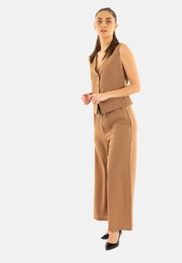 Top senza maniche color tan con bottoni abbinato a pantaloni ampi, entrambi in un tessuto morbido. Tacchi neri a punta completano l'outfit.