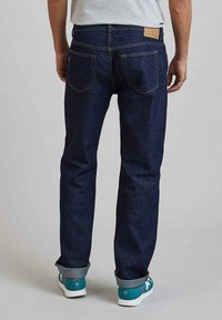 Donkerblauwe denim jeans met een rechte pijp, met achterzakken, een gestikt ontwerp en opgerolde boorden. Gecombineerd met teal sneakers.