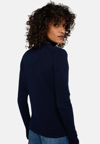 Pull en tricot bleu marine à manches longues avec un col montant et un motif texturé. Il présente des manches ajustées et un ourlet légèrement arrondi.