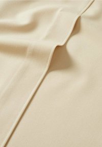 Tissu beige avec une couture surpiquée créant un pli doux et une ombre, mettant en valeur la texture et la surface lisse du matériau.