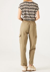 Beige cargo pants with a relaxed fit, featuring side pockets and an elastic waistband, paired with a patterned short-sleeve top.
