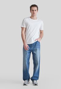Camiseta blanca de manga corta, vaqueros de mezclilla azules holgados con desgaste, y zapatillas deportivas grises. Diseño sencillo, ajuste casual, y sin patrones visibles.