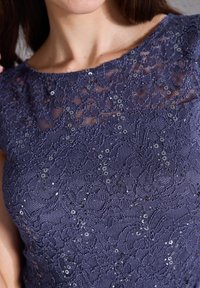 Top en dentelle bleu marine présentant des motifs floraux complexes, des paillettes et un col rond, avec un tissu texturé pour plus de dimension.