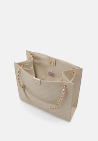 Beżowa pikowana torba na ramię z podwójnymi łańcuszkami i tkaninowymi uchwytami. Wnętrze ozdobione złotymi akcentami oraz subtelną metką z logo. Zamyka się na zatrzask.