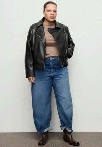 Czarna skórzana kurtka biker, beżowa dopasowana bluzka, luźne niebieskie jeansy z mankietami oraz brązowe botki za kostkę. Proste, nowoczesne elementy designu.