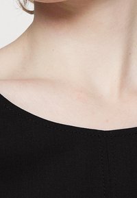 Close-up of neck and collarbone area wearing a black garment with visible stitching along the neckline.