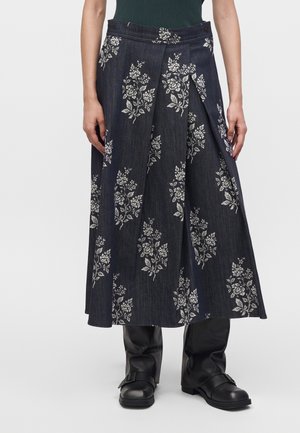 Falda midi de mezclilla oscura con estampados florales blancos, usada con botas negras con hebilla y una camiseta sin mangas verde oscuro.