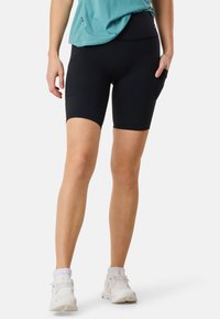 Pantaloni da ciclismo neri realizzati in tessuto elastico, con vita alta e tasche laterali, abbinati a scarpe sportive bianche.