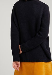Navy knitted sweater with a relaxed fit, featuring long sleeves and ribbed cuffs, paired with a mustard yellow skirt.