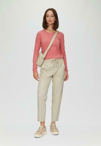Lichtroze langemouwtop gecombineerd met beige tapered broek en beige sneakers, met een drawstring taille en een kleine schoudertas.