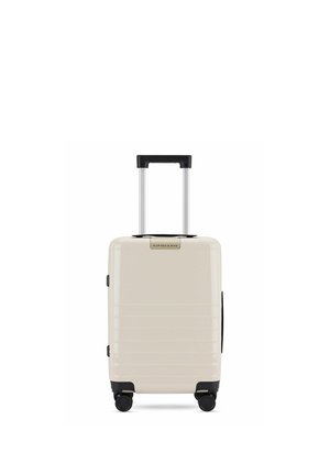 Valise compacte beige à coque rigide avec poignée télescopique et quatre roues noires multidirectionnelles, marque « Kapten & Son » à l'avant.