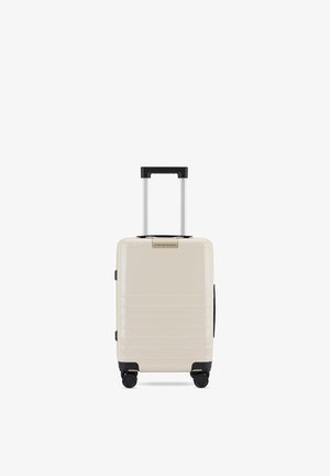 Valise compacte beige à coque rigide avec poignée télescopique et quatre roues noires multidirectionnelles, marque « Kapten & Son » à l'avant.