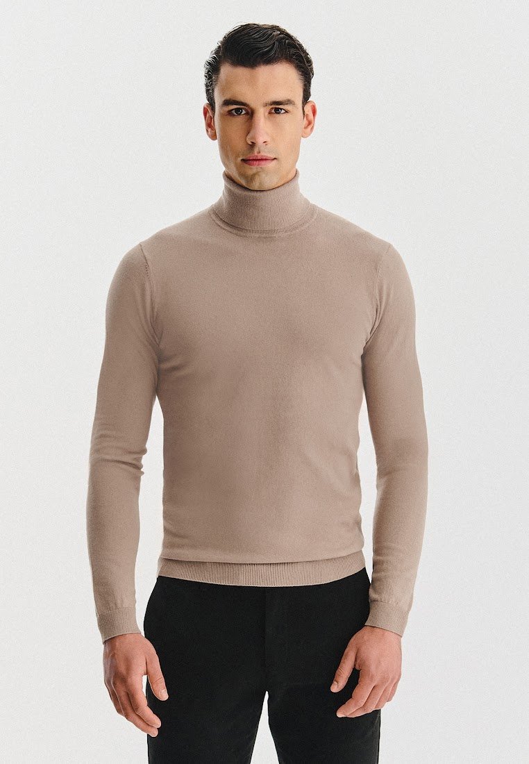 Beżowy sweter z golfem wykonany z miękkiego dzianinowego materiału. Dopasowany fason z prążkowanymi mankietami i dołem, noszony z ciemnymi spodniami. Gładka faktura.