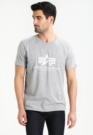 T-shirt en coton gris à manches courtes, avec un design graphique blanc du nom de la marque "Alpha Industries" et un logo.
