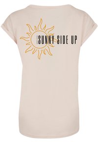 Light pink t-shirt featuring a yellow sun graphic and black text reading "KEEP YOUR SUNNY SIDE UP." Soft fabric with rolled sleeves.