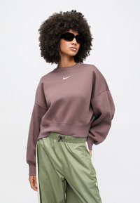 Μακριά μπορντό φούτερ με λευκό λογότυπο Nike, συνδυασμένο με πράσινο, ελαφρύ παντελόνι με ελαστική μέση, πλαϊνές ρίγες και τσέπες.