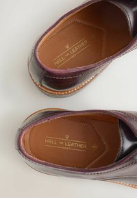 Pantofi slip-on din piele burgund cu o textură netedă, margini cusute și un logo auriu pe brantul maro. Formă rotundă și design cu profil mic.