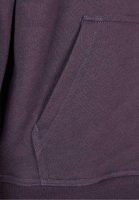 Tissu de sweat-shirt violet montrant un détail de poche avec des surpiqûres visibles et un ourlet côtelé. La texture semble douce et confortable.