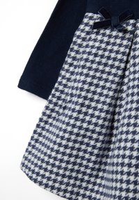Top a maglia blu navy e gonna a fantasia houndstooth nelle tonalità di blu e bianco, con un piccolo fiocco blu navy sulla vita.