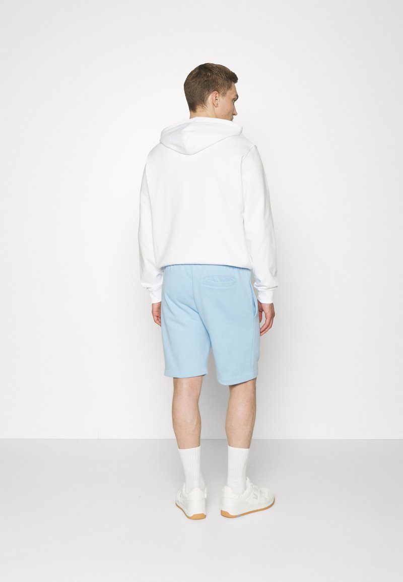 Haut à capuche blanc associé à un short bleu clair. Cette tenue présente une coupe décontractée et est fabriquée en tissu doux et léger.