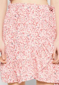 Gonna a stampa floreale di un rosa tenue, con orlo ondulato e dettaglio con fiocco laterale. Realizzata in tessuto leggero con delicati accenti e motivi neri.