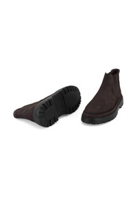 Bottines en daim marron avec une finition texturée, des panneaux latéraux élastiques et une semelle en caoutchouc noir robuste. Détails cousus le long des bords.