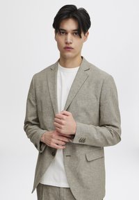 Ljust brunt linneblazer med en skräddarsydd passform, en ficka och knappstängning. Bärs över en enkel vit t-shirt. Texturerat tyg.