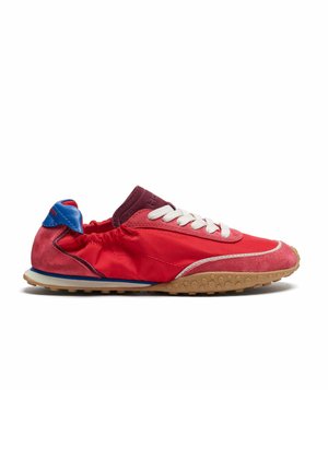 Zapatilla ligera roja y burdeos con cordones blancos, lengüeta azul en el talón y suela texturizada beige sobre un fondo blanco liso.