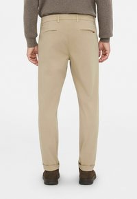 Pantalones beige de corte recto, con dos bolsillos traseros y puños enrollados. El material parece suave con un ligero brillo.