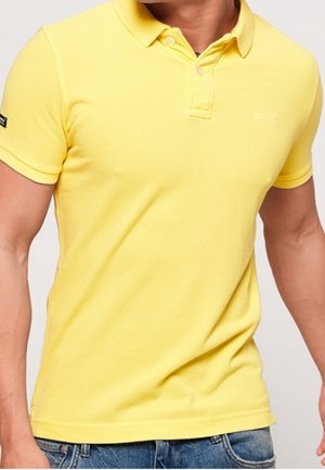 Yellow cotton polo shirt with a collar and two buttons, featuring a small logo on the chest. Short sleeves with a smooth texture.