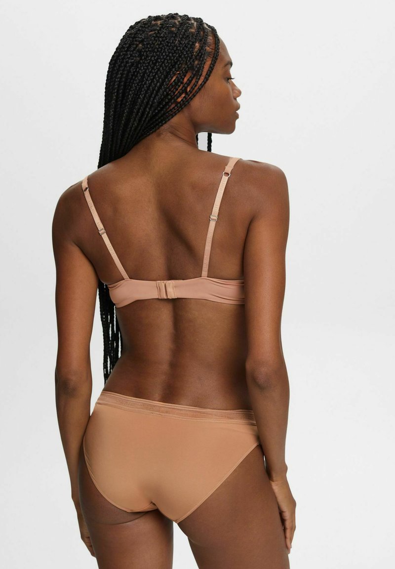 Hautfarbener Dessous-Satz mit einem nahtlosen BH mit verstellbaren Trägern und Hakenverschluss, kombiniert mit passenden kniehohen Bikini-Unterhosen.