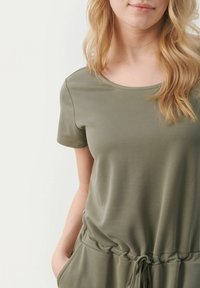 Top de manga corta verde oliva hecho de una tela suave, con un escote redondeado y una cintura con cordón para un ajuste ajustable.
